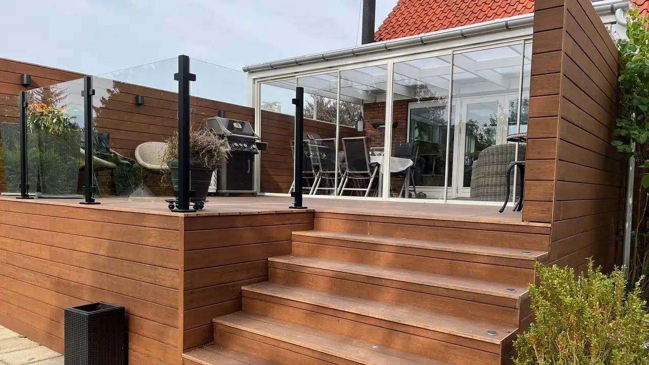 Glasgelænder med sorte stolper ved udendørstrappe og terrasse med niveauforskel.