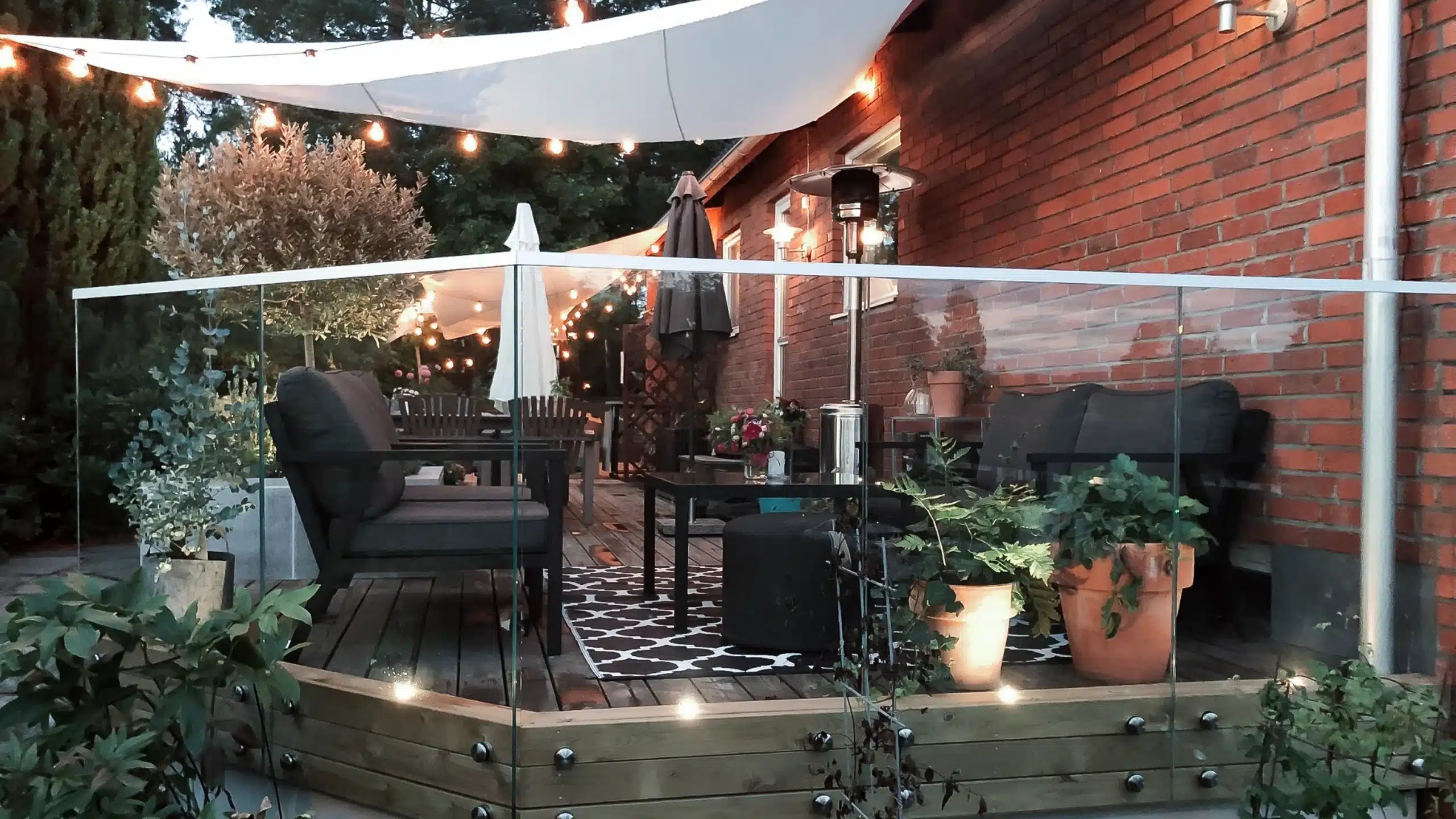 Glasgelænder på terrasse i aftenlys med belysning langs terrassen.