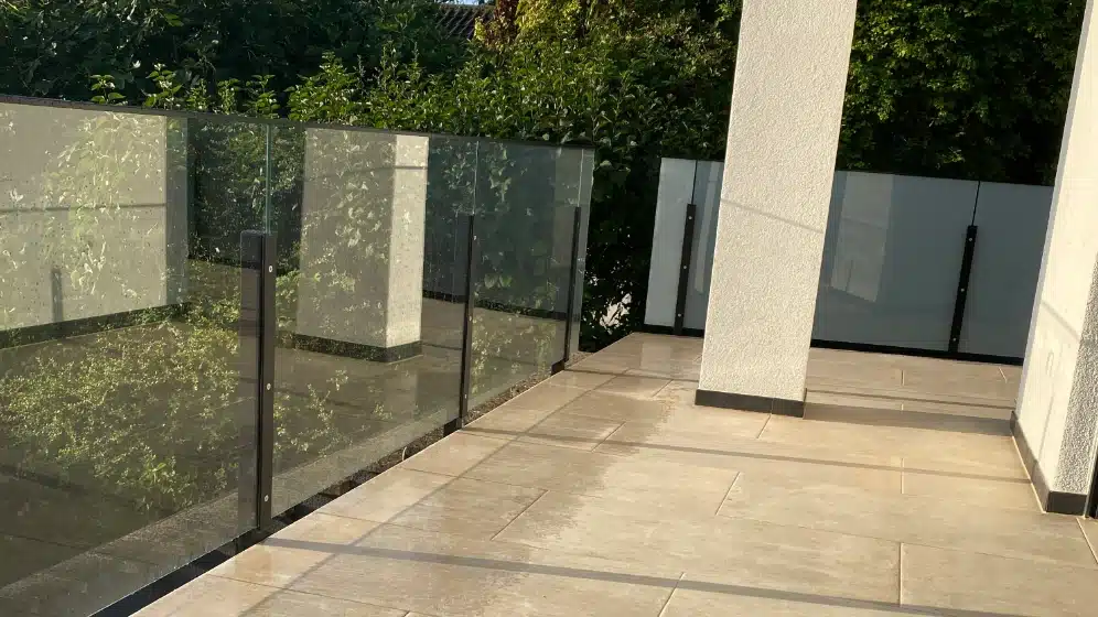 Glasgelænder med tonet glas på en terrasse ved en hvid facade.