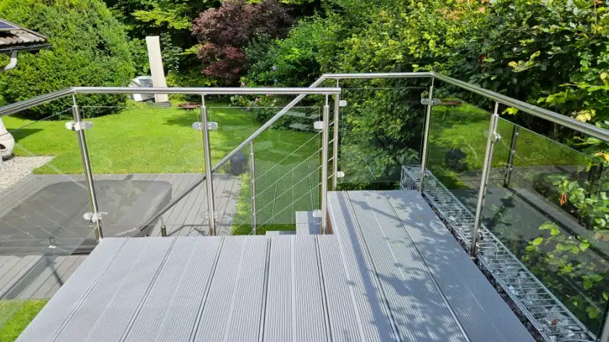 Glasgelænder med håndliste ved udendørstrappe og terrasse i en have.