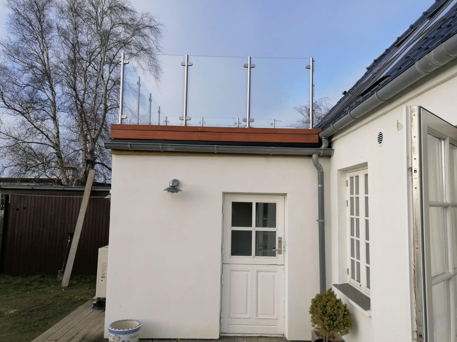Glasgelænder på et fladt tag til et hvidt hus med » fastgørelse « langs tagkanten.