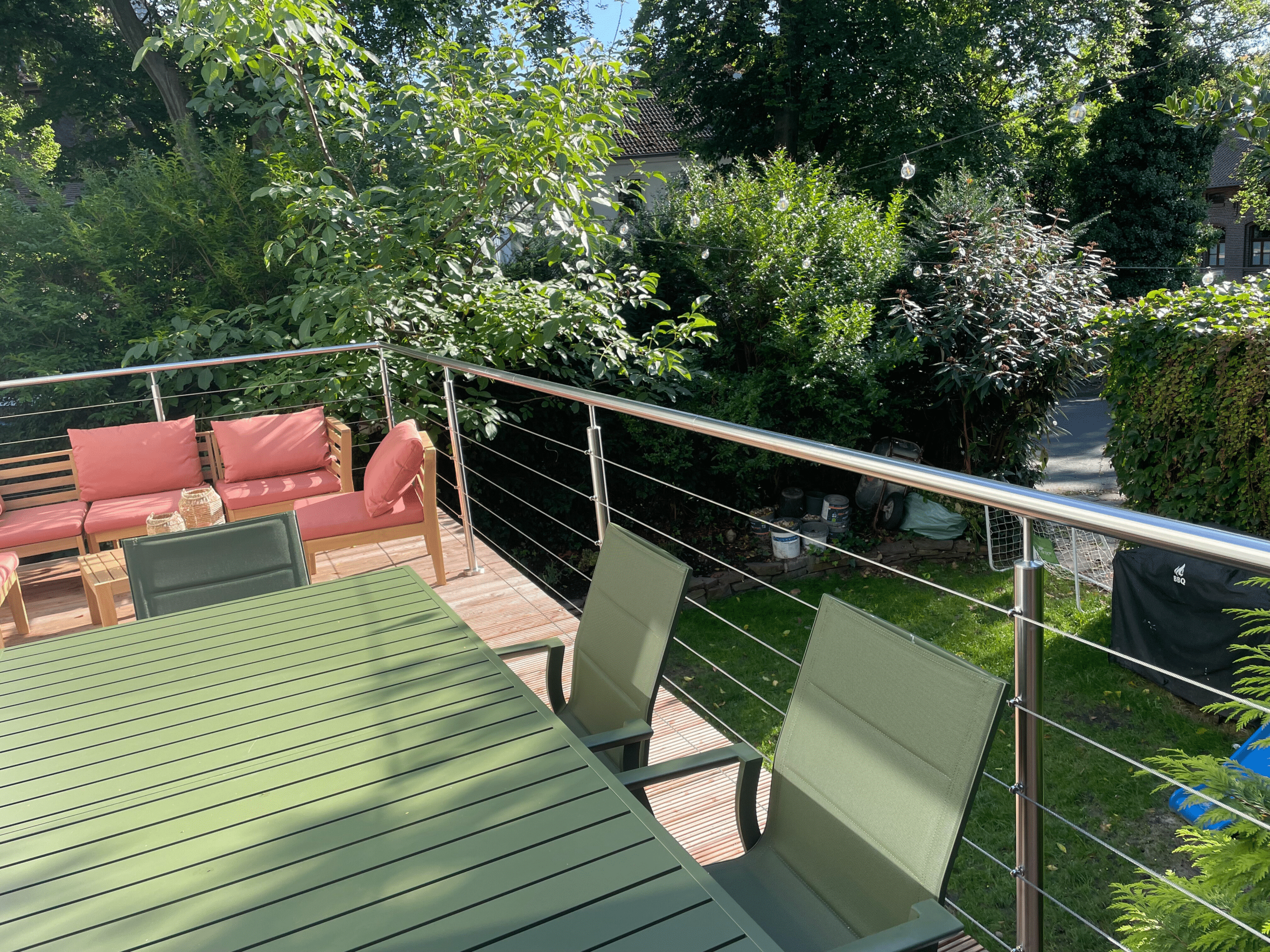 Stor møbleret terrasse med spisebord, grønne planter og wiregelænder , der indrammer altanen.